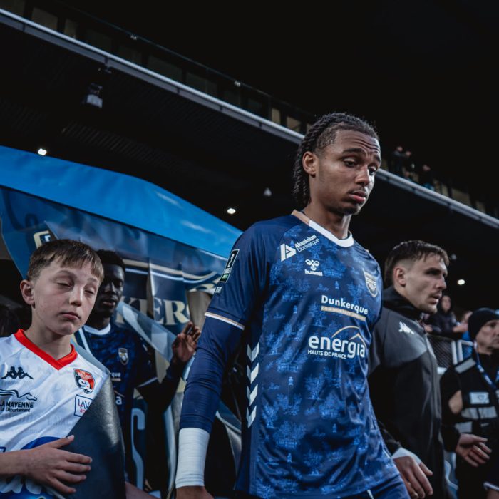 A USL Dunkerque player walking onto the pitch with a young mascot