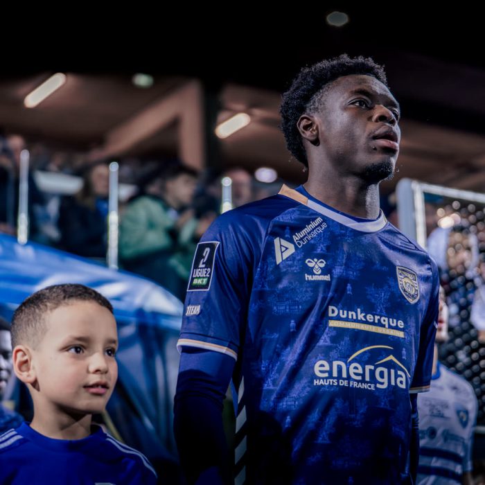 A USL Dunkerque player standing beside a young supporter before the match