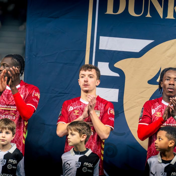 Three USL Dunkerque players applauding in front of the club banner